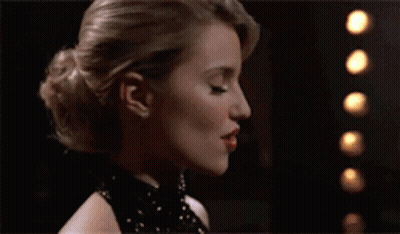 A Woman In A Black Dress Is Standing Next To A Pizza GIF