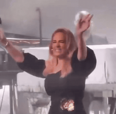 A Woman In A Black Dress Is Standing On A Stage With Her Arms In The Air . GIF