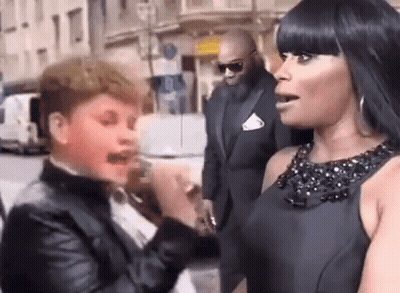 A Woman In A Black Dress Is Talking To A Boy In A Tuxedo On The Street . GIF