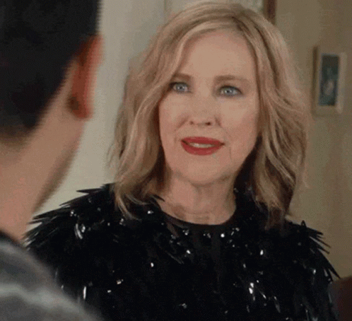 A Woman In A Black Dress Is Talking To A Man In A Room . GIF