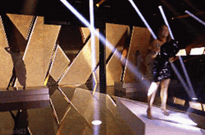 A Woman In A Black Dress Is Walking Down A Stage GIF
