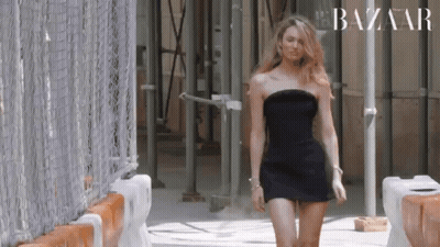 A Woman In A Black Dress Is Walking Down A Street . GIF