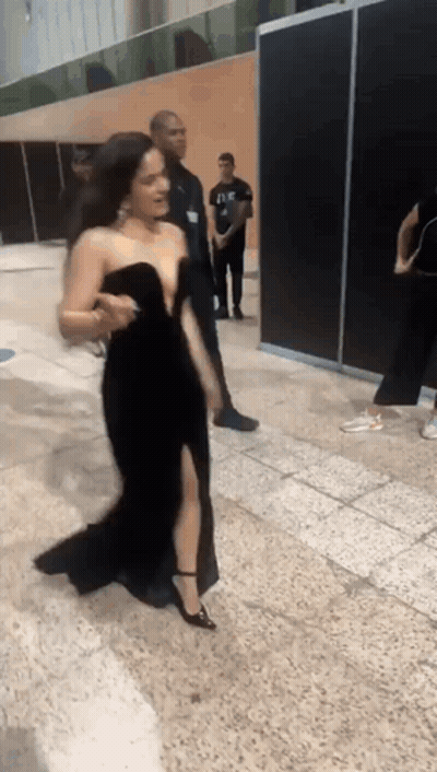 A Woman In A Black Dress Is Walking On A Tiled Floor GIF