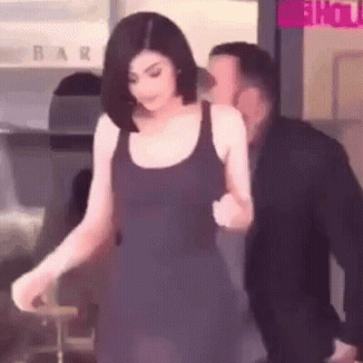 A Woman In A Black Dress Is Walking With A Man In A Suit Behind Her . GIF