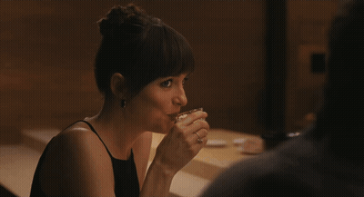 A Woman In A Black Dress Sits At A Table GIF