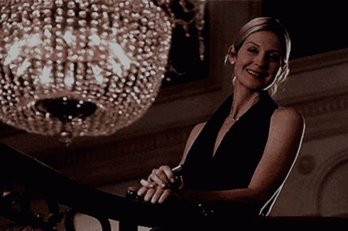 A Woman In A Black Dress Smiles While Sitting On A Staircase GIF