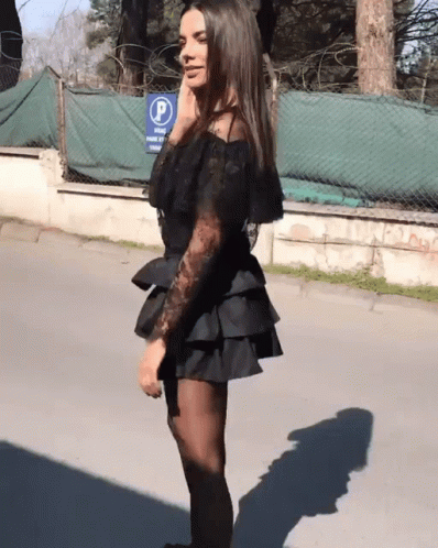 A Woman In A Black Dress Stands In Front Of A Blue Sign That Says " Park " GIF