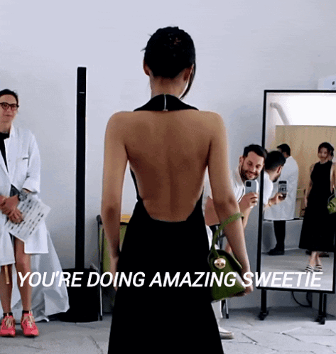 A Woman In A Black Dress Stands In Front Of A Mirror With The Words " You 'Re Doing Amazing Sweetie " GIF
