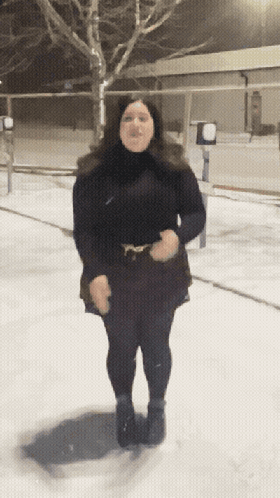 A Woman In A Black Dress Stands In The Snow GIF