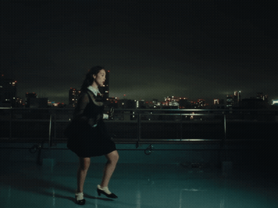 A Woman In A Black Dress Stands On A Rooftop At Night GIF