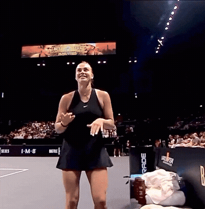 A Woman In A Black Dress Stands On A Tennis Court In Front Of A Large Screen That Says I-M-8 GIF