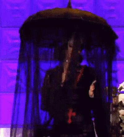 A Woman In A Black Dress With A Cross Around Her Neck Is Holding An Umbrella . GIF
