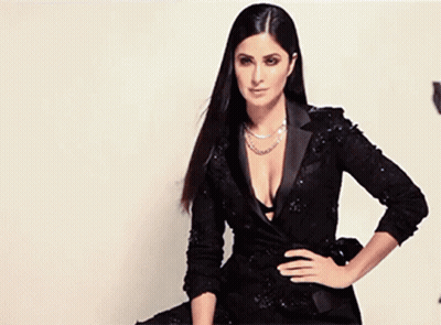 A Woman In A Black Dress With A Plunging Neckline Is Sitting On A Chair . GIF