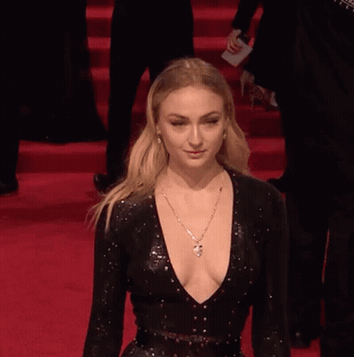 A Woman In A Black Dress With A Plunging Neckline Is Walking Down A Red Carpet . GIF