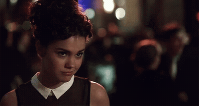 A Woman In A Black Dress With A White Collar Looks At The Camera GIF