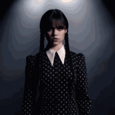A Woman In A Black Dress With White Polka Dots And Braids GIF