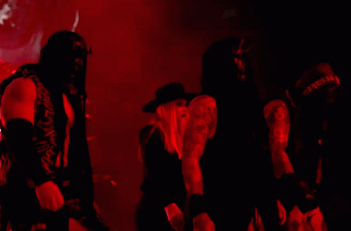 A Woman In A Black Hat Is Standing Next To A Man In A Black Shirt That Says ' Slayer ' GIF