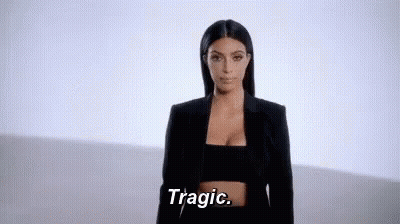 A Woman In A Black Jacket And Crop Top Is Standing In Front Of A White Wall And Saying Tragic . GIF