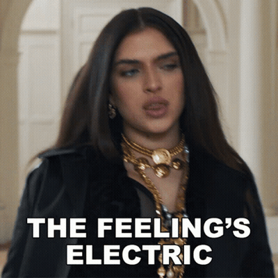 A Woman In A Black Jacket And Gold Necklace Says " The Feeling 'S Electric " In White Letters GIF