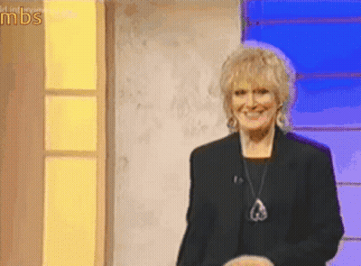 A Woman In A Black Jacket And Necklace Is Smiling On A Stage In Front Of A Sign That Says Mds GIF