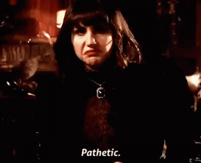 A Woman In A Black Jacket And Necklace Is Standing In A Dark Room And Talking . GIF