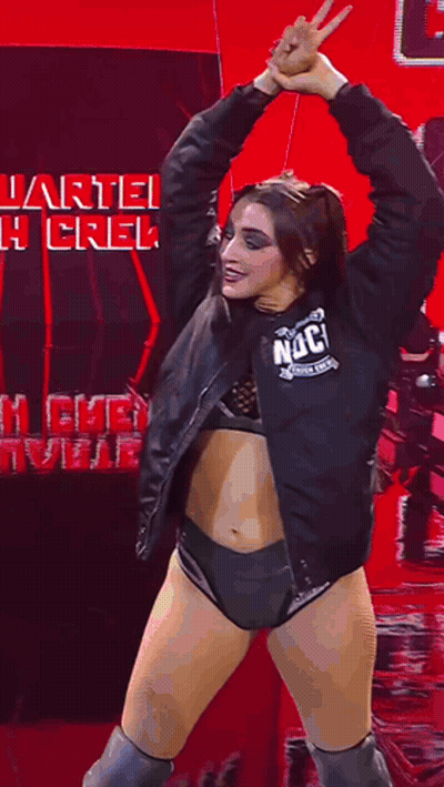 A Woman In A Black Jacket And Shorts Is Dancing In Front Of A Sign That Says Quarterback Crew . GIF
