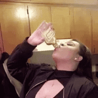 A Woman In A Black Jacket Is Drinking From A Bottle Of Beer . GIF