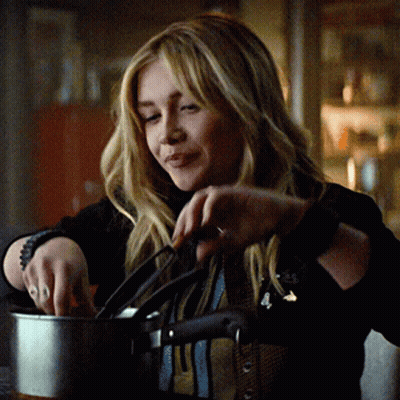 A Woman In A Black Jacket Is Holding A Pot And Smiling GIF