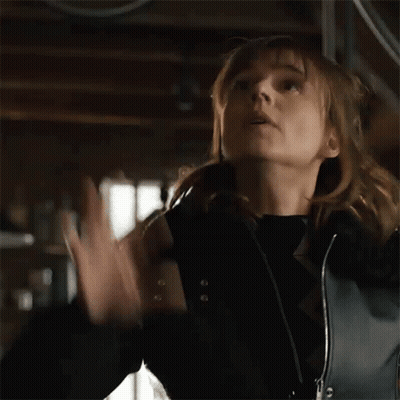 A Woman In A Black Jacket Is Holding Her Hands Up In The Air GIF