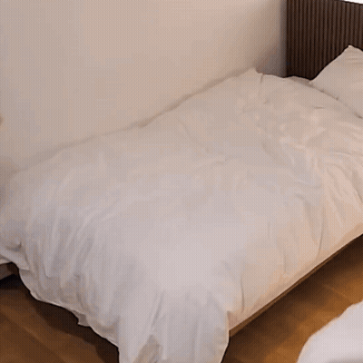 A Woman In A Black Jacket Is Making A Bed . GIF