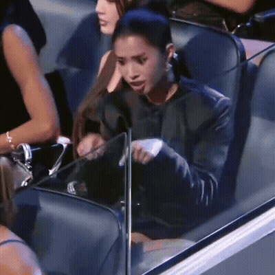 A Woman In A Black Jacket Is Sitting In A Stadium Holding A Piece Of Paper . GIF