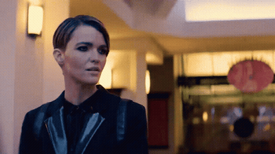 A Woman In A Black Jacket Is Standing In A Building GIF