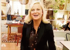 A Woman In A Black Jacket Is Standing In A Living Room Laughing . GIF