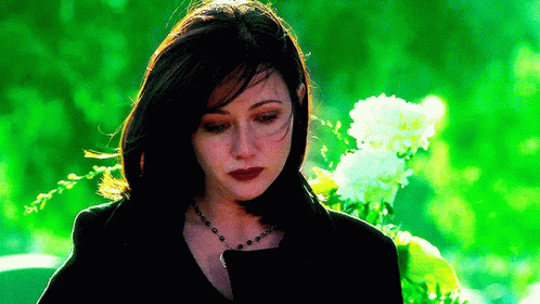 A Woman In A Black Jacket Is Standing In Front Of A Bouquet Of Flowers . GIF