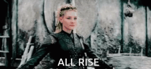 A Woman In A Black Jacket Is Standing In Front Of A Wall With The Words `` All Rise '' . GIF