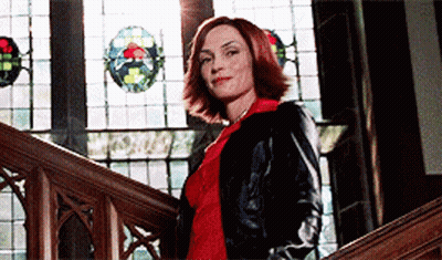 A Woman In A Black Jacket Is Standing On A Set Of Wooden Stairs In Front Of A Stained Glass Window GIF