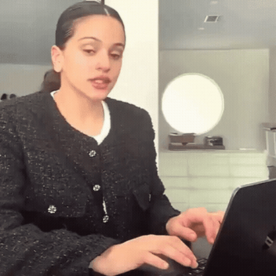 A Woman In A Black Jacket Is Using A Laptop Computer . GIF