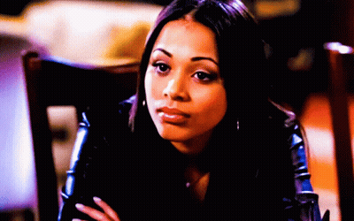 A Woman In A Black Jacket Sits In A Chair With Her Hands Folded GIF
