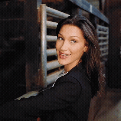 A Woman In A Black Jacket Smiles In Front Of A Metal Fence GIF
