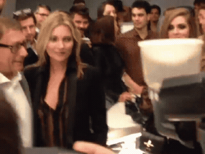 A Woman In A Black Jacket Stands In A Crowd GIF