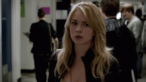 A Woman In A Black Jacket Stands In A Hallway Looking At The Camera GIF