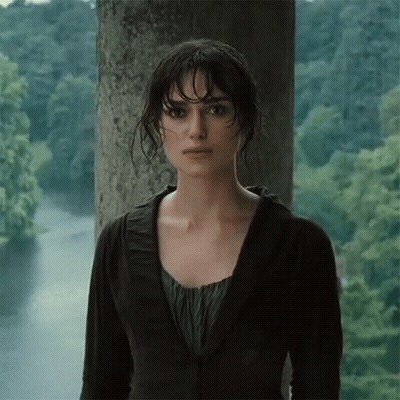 A Woman In A Black Jacket Stands In Front Of A Body Of Water GIF