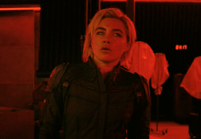A Woman In A Black Jacket Stands In Front Of A Red Sign That Says ' Gen ' GIF
