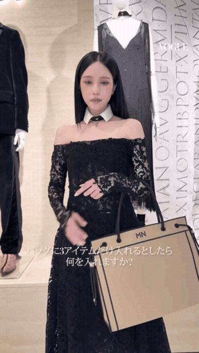 A Woman In A Black Lace Dress Is Holding A Bag That Says Mn On It GIF