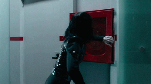 A Woman In A Black Latex Suit Is Reaching For A Red Fire Hydrant GIF