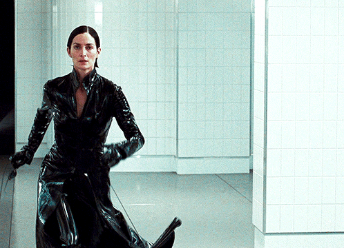 A Woman In A Black Latex Suit Is Standing In A Hallway GIF
