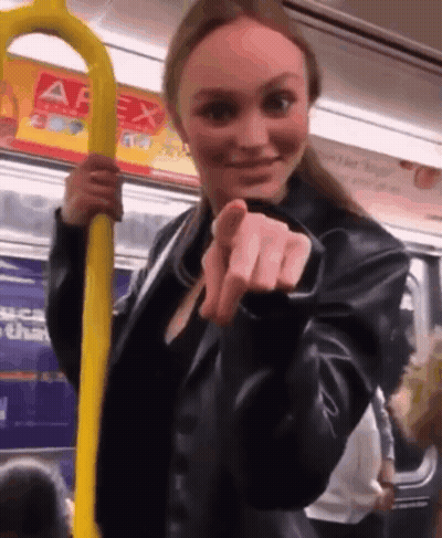 A Woman In A Black Leather Jacket Is Holding A Yellow Railing On A Subway Train . GIF