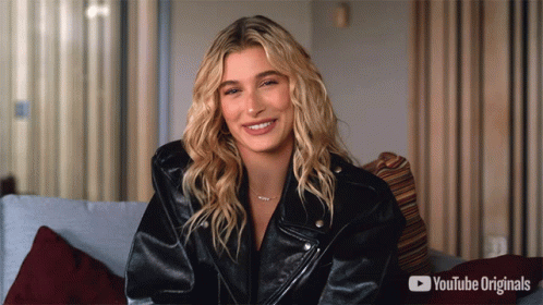 A Woman In A Black Leather Jacket Is Smiling In Front Of A Youtube Originals Advertisement GIF