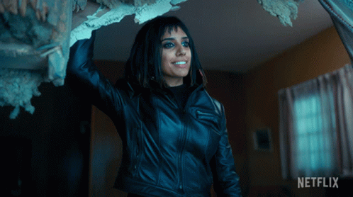 A Woman In A Black Leather Jacket Is Standing In A Room With A Netflix Logo On The Bottom GIF