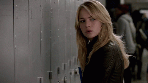 A Woman In A Black Leather Jacket Is Standing In Front Of A Row Of Lockers GIF